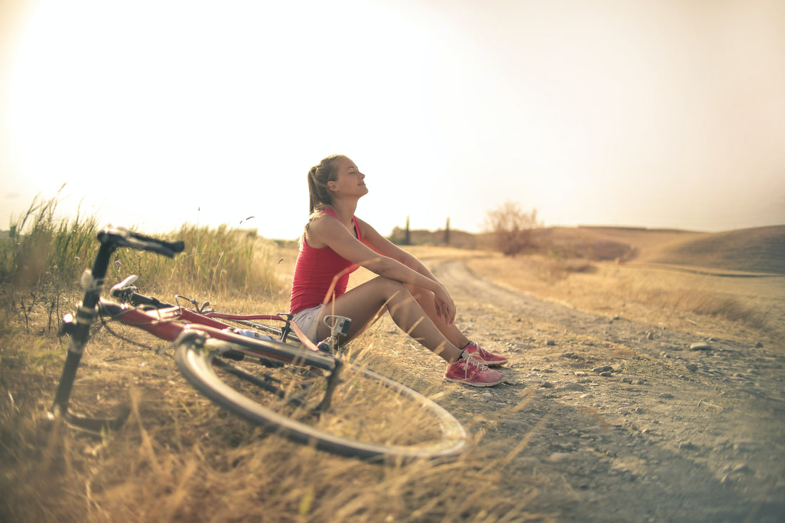 young woman sitting in the grass beside her bicycle to cool off during the summer